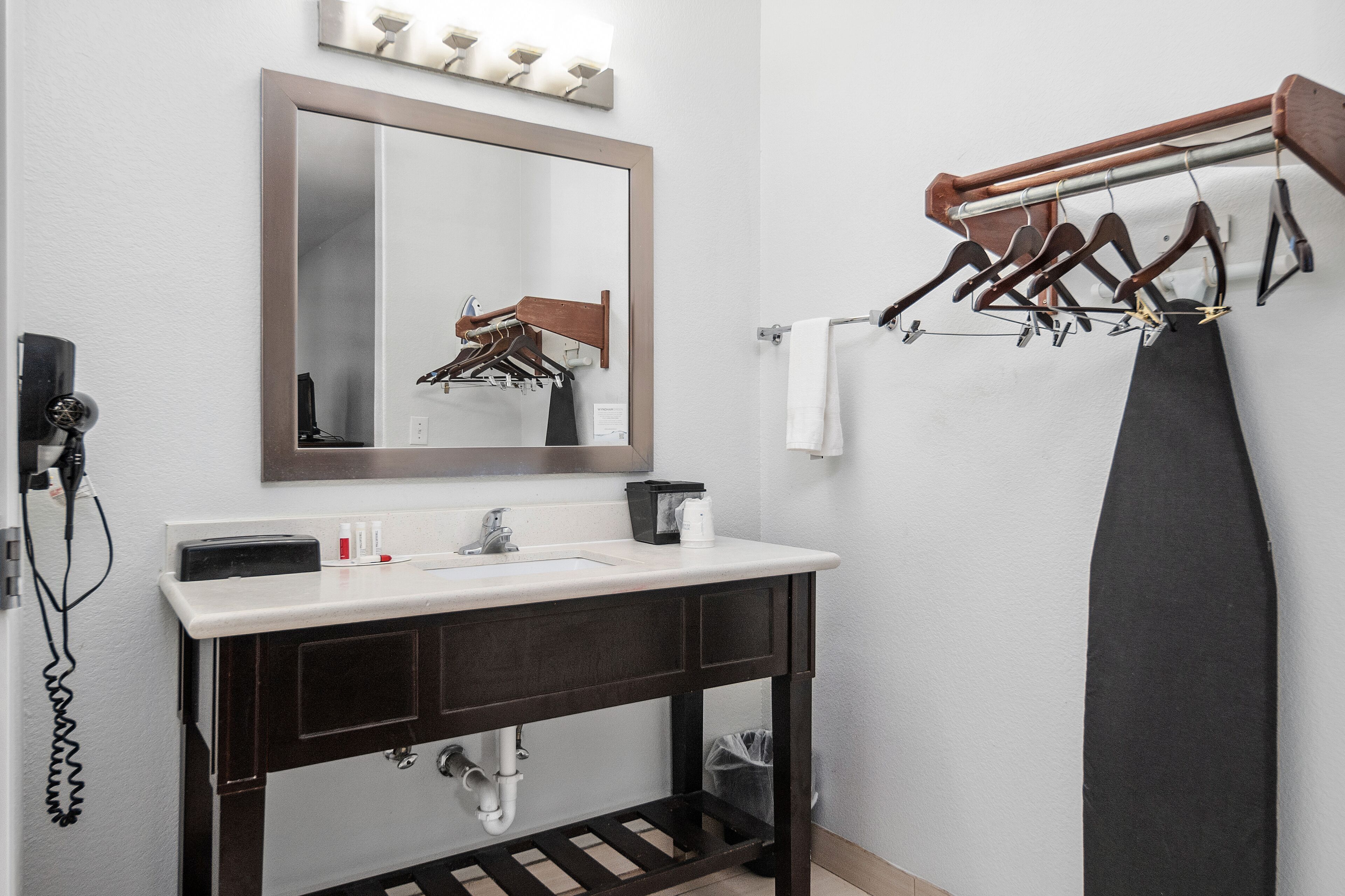 A bathroom with a sink, mirror, towel rack, and a hairdryer on the wall.