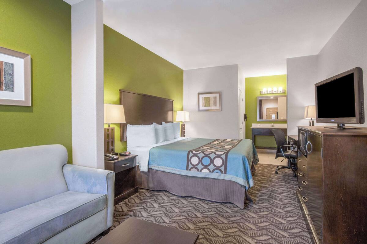 A hotel room with a bed, a desk, a chair, a television, and a couch.