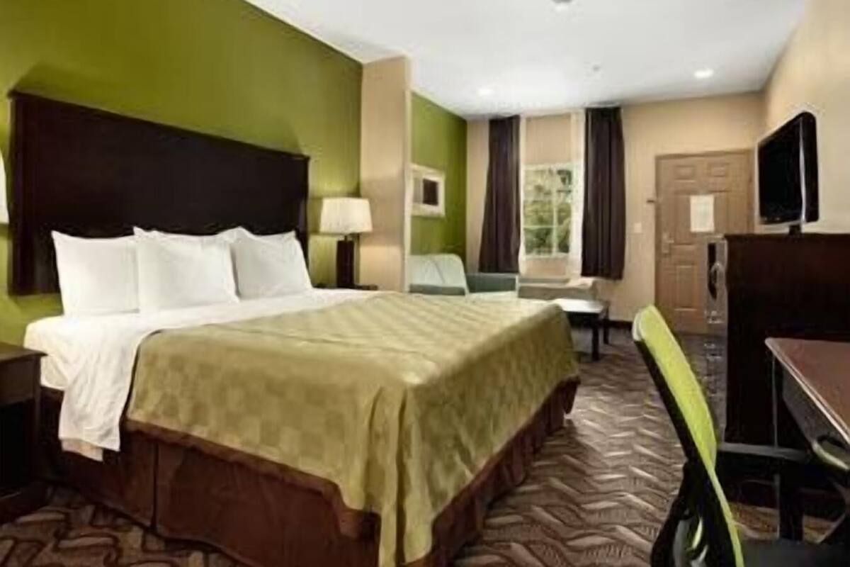 A hotel room with a bed, a desk, a chair, a TV, and a window with curtains.
