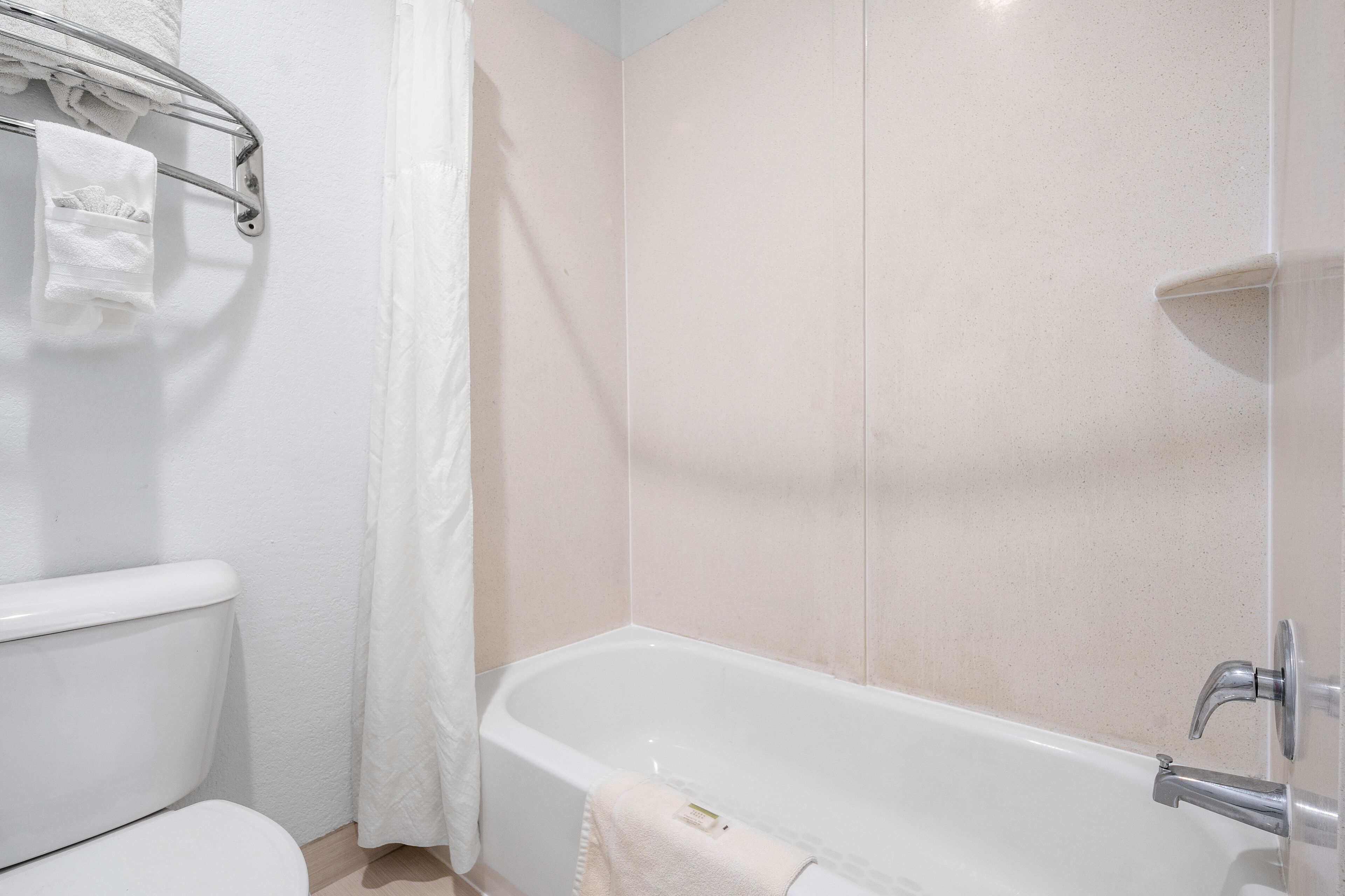 A bathroom with a white bathtub, a toilet, and a towel rack with a towel.