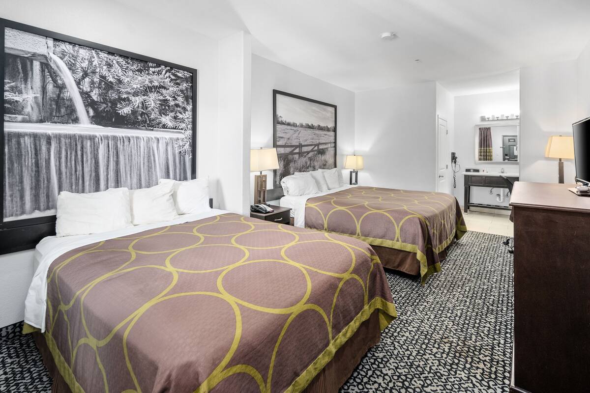 A hotel room with two beds, a desk, a chair, a TV, and a bathroom visible through an open door.