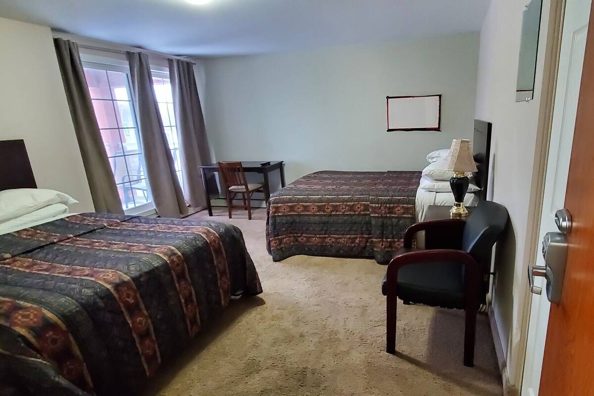 A hotel room with two beds, a desk, a chair, a lamp, and a window with curtains.
