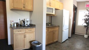 A kitchen with wooden cabinets, a microwave, a refrigerator, a coffee maker, and a trash can. - Budget Lodge (Saskatoon)