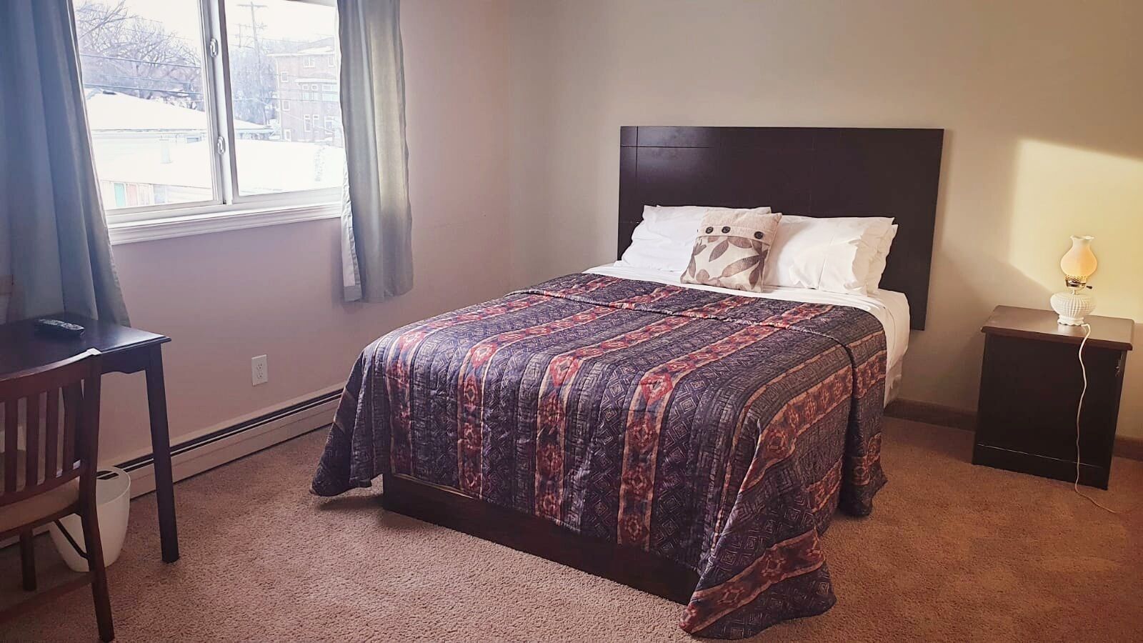 A bedroom with a bed, a nightstand, a chair, and a window.