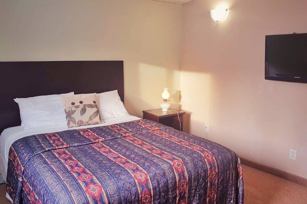 A hotel room with a bed, a nightstand, a lamp, and a wall-mounted TV.