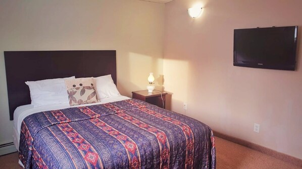 A hotel room with a bed, a nightstand, a lamp, and a wall-mounted TV. - Budget Lodge (Saskatoon)