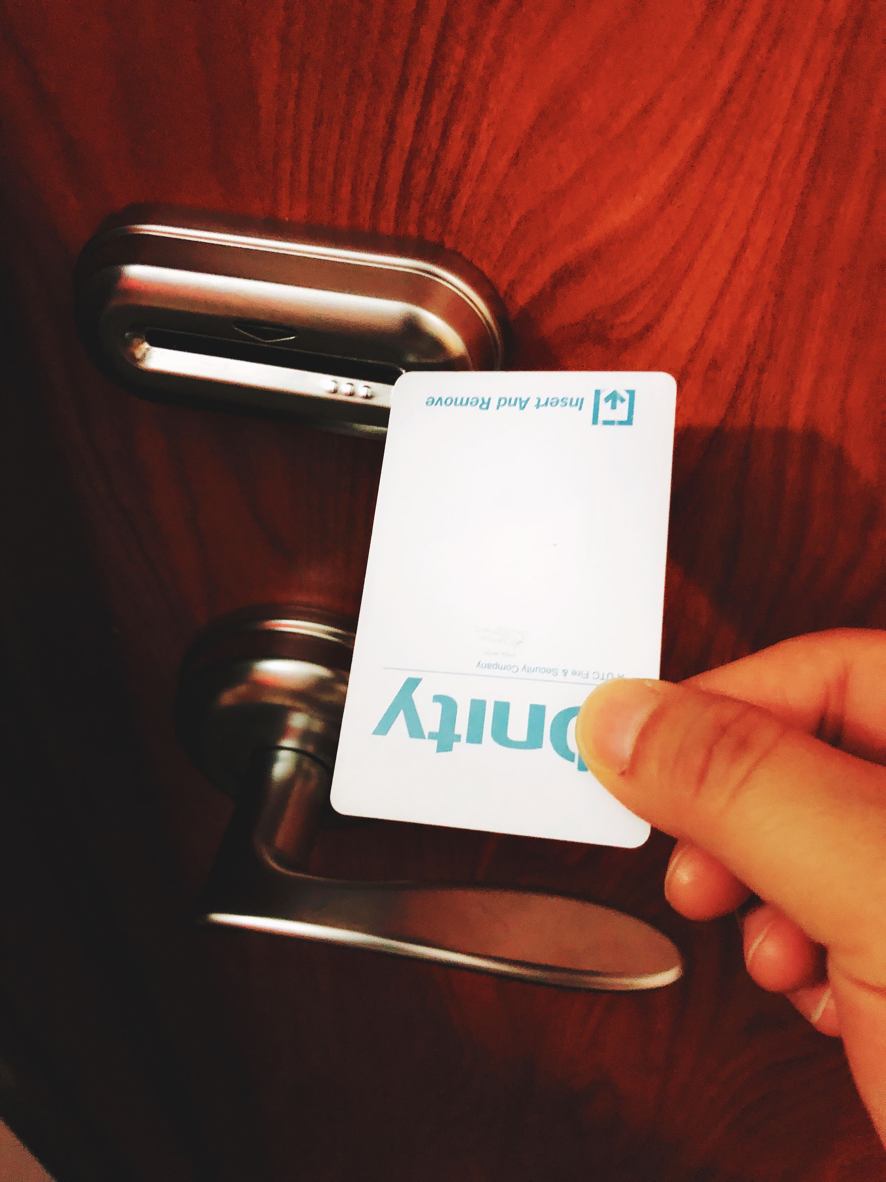 A hand holding a card with the word "Dutty" on it, placed on a metallic door handle.
