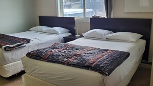 A hotel room with two single beds, a large window, and a view of the outside. - Budget Lodge (Saskatoon)