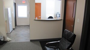 A hotel lobby with a reception desk, a waiting area with a leather chair, a refrigerator, and a door with an exit sign. - Budget Lodge (Saskatoon)