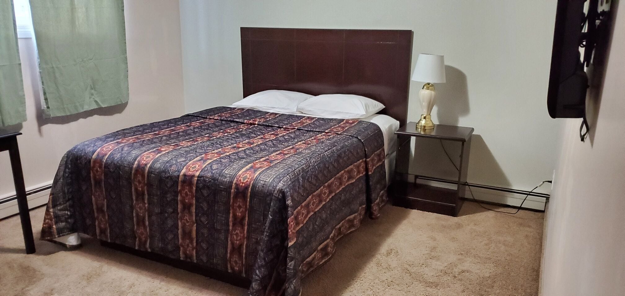 A bed with a patterned bedspread, a bedside table with a lamp, and a wall-mounted TV.