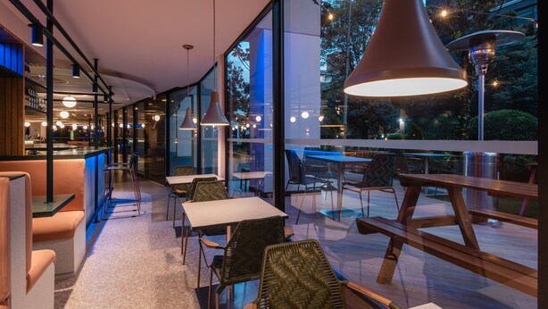 A modern restaurant with glass walls, indoor and outdoor seating, and pendant lighting. - Novotel Bogotá Parque 93 (Bogotá)