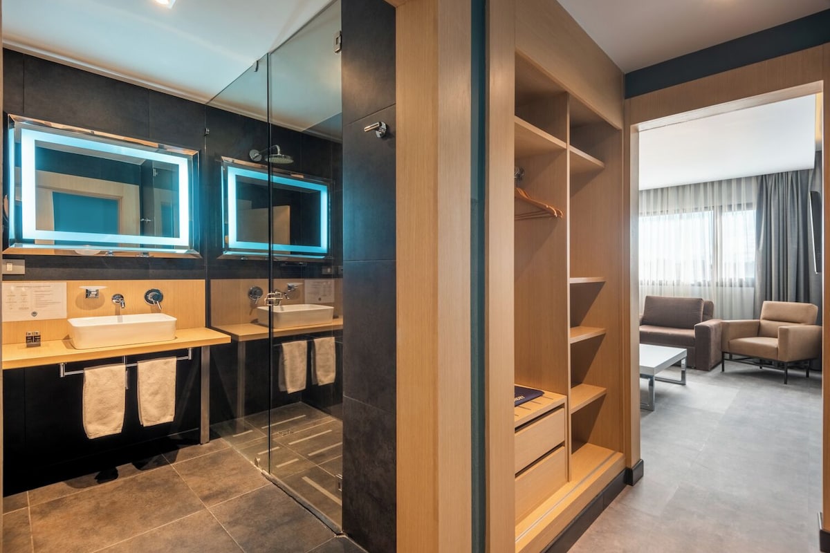 A modern bathroom with a glass-enclosed shower, dual sinks, and a vanity with a mirror.