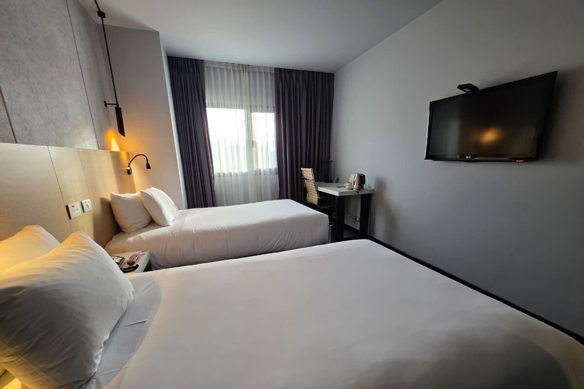 A hotel room with two beds, a desk, a TV, and a window with curtains.