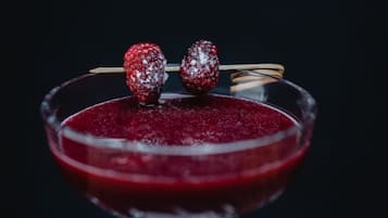 Una copa de martini con una bebida rojo oscuro y dos frambuesas ensartadas en un palillo.