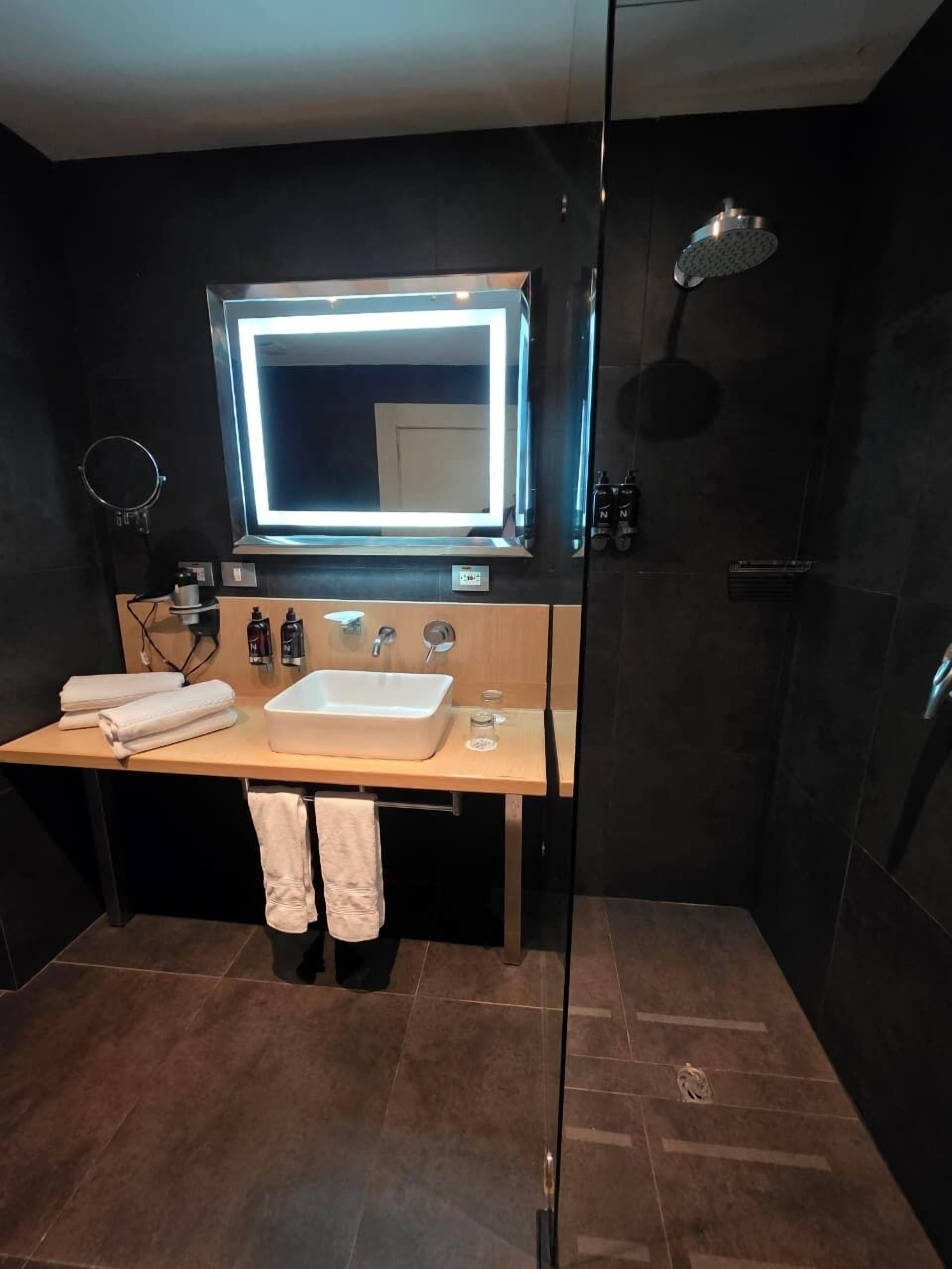 A modern bathroom with a large mirror, a sink, and a shower.