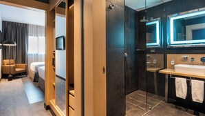 A modern hotel room with a walk-in closet, a separate bathroom with a glass shower enclosure, and a large mirror above the sink. - Novotel Bogotá Parque 93 (Bogotá)