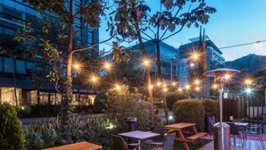 An outdoor patio area with wooden tables and chairs, string lights, and a metal heater. - Novotel Bogotá Parque 93 (Bogotá)