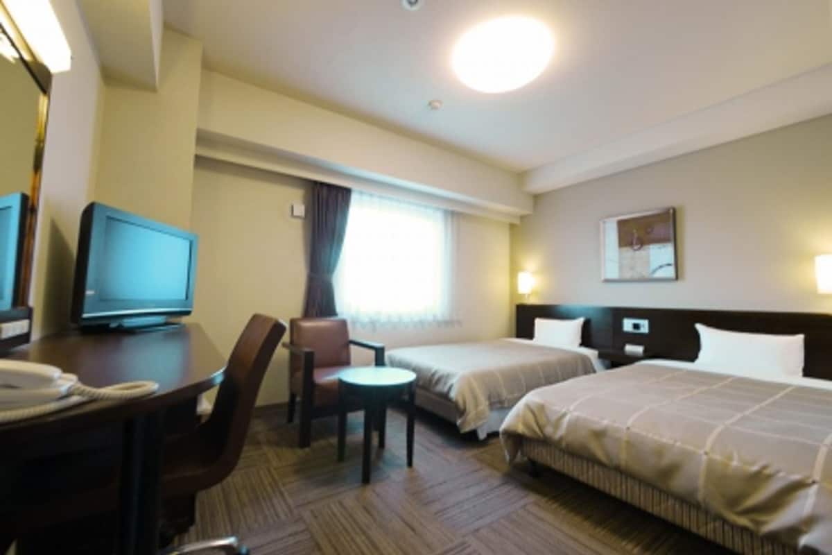 A hotel room with two beds, a desk with a telephone, a chair, and a television.