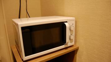 A white microwave on a wooden shelf in a room with beige walls.