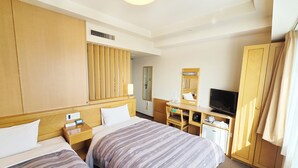 Ein Hotelzimmer mit zwei Betten, einem Schreibtisch mit Fernseher, einem Spiegel und einem Kleiderschrank.