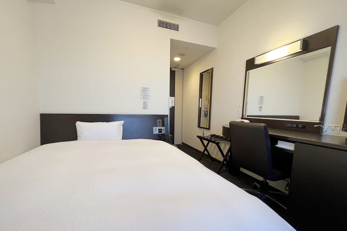 A hotel room with a large bed, a desk with a chair, a mirror, and a small table.