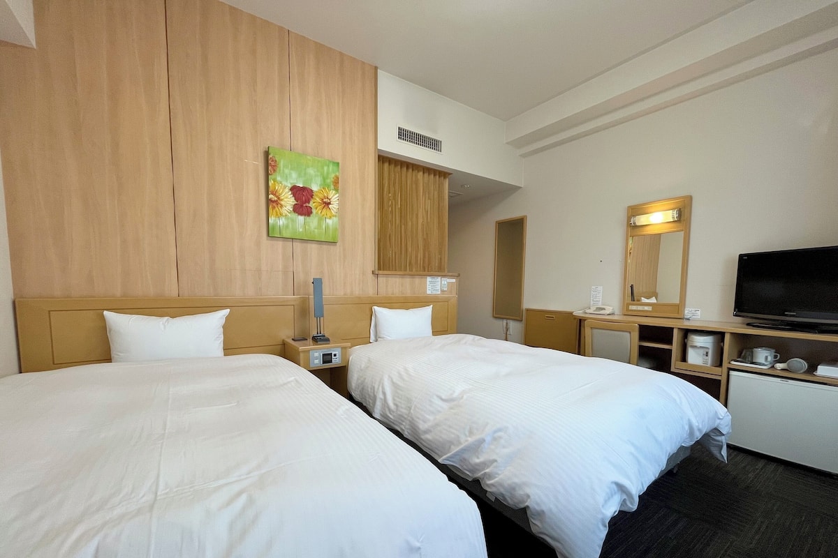 A hotel room with two beds, a TV, a desk with a mirror, and a painting on the wall.