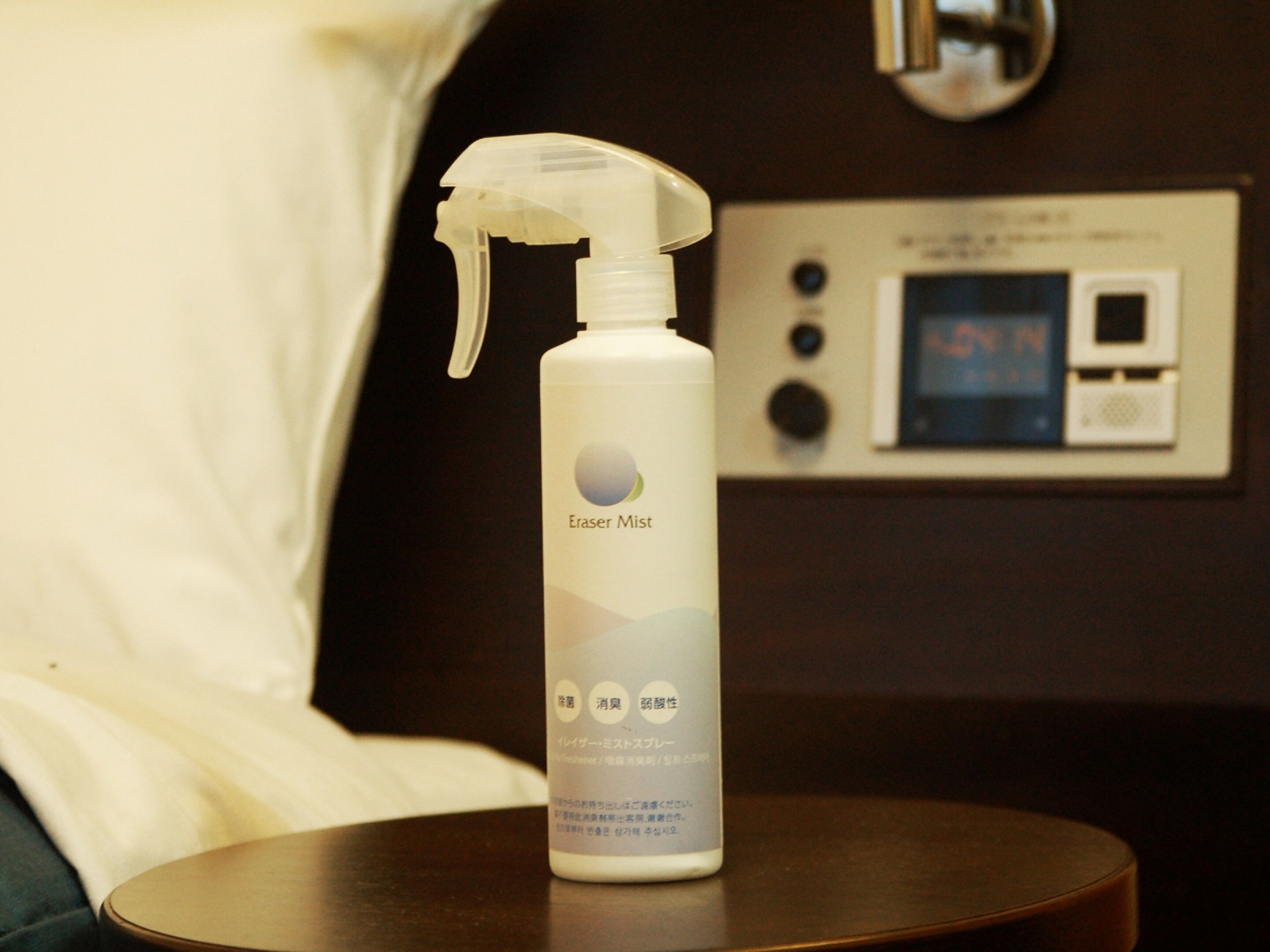 A bottle of Eraser Mist on a bedside table in a hotel room.