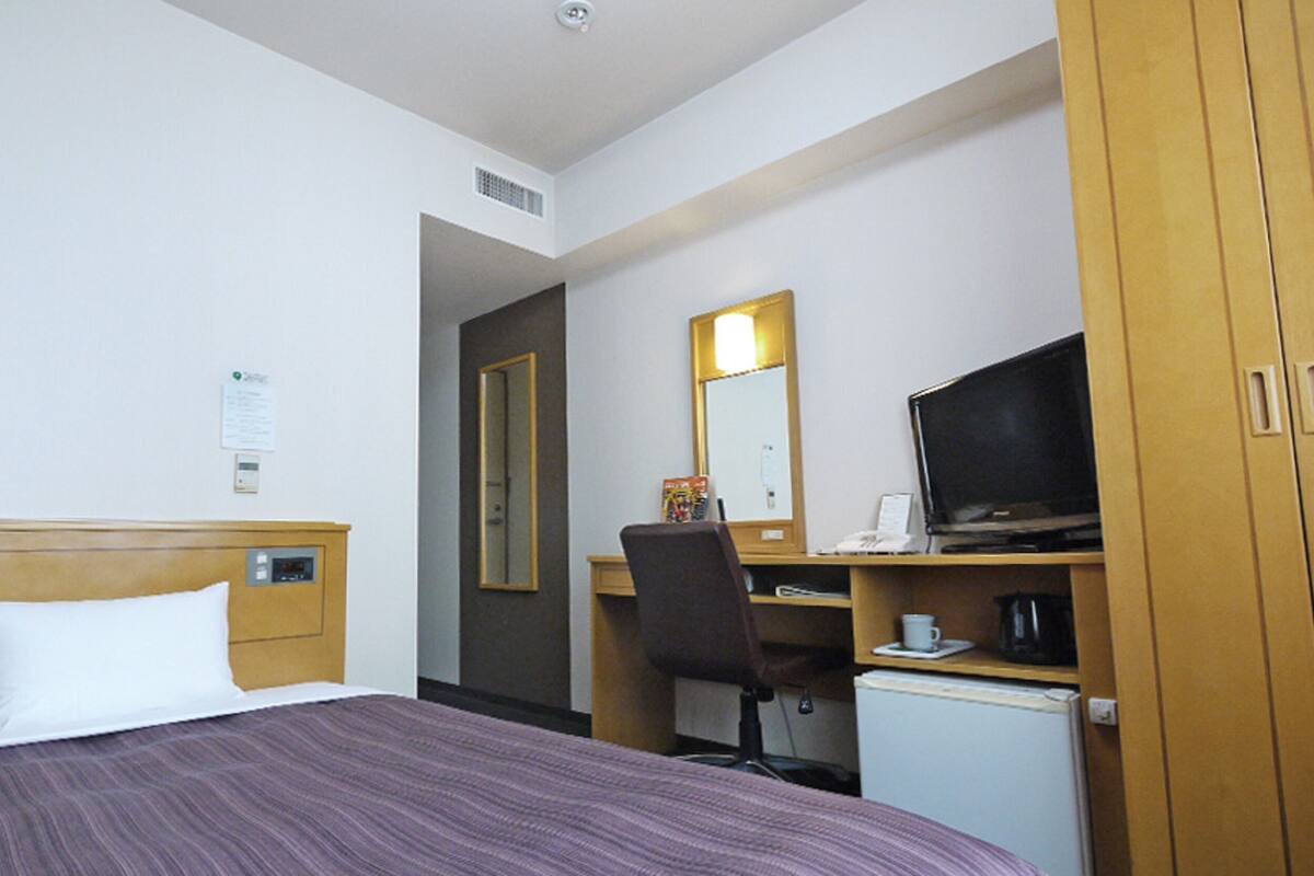 A hotel room with a bed, a desk with a computer, a television, and a small refrigerator.