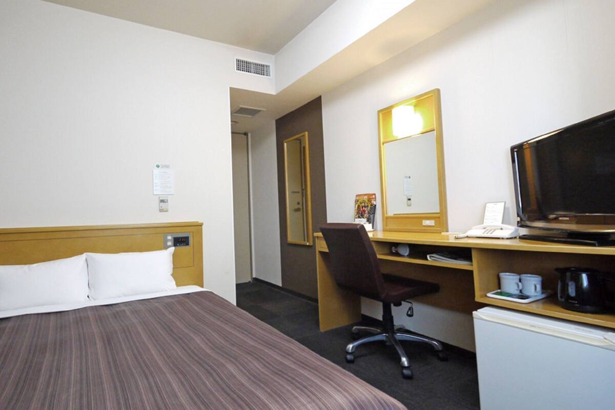 A hotel room with a bed, a desk with a chair, a television, and a coffee maker.