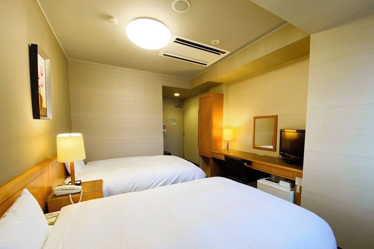 Une chambre d’hôtel avec deux lits, un bureau, une chaise, une télévision et une lampe.
