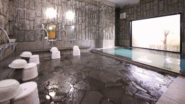 Un espacio interior con piscina de paredes de piedra, una ventana grande, una sauna y varios baños.