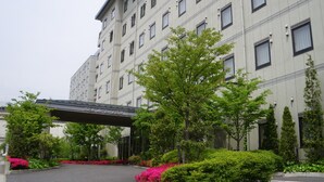 Un hotel de varios pisos con entrada cubierta, rodeado de follaje y plantas florecientes.