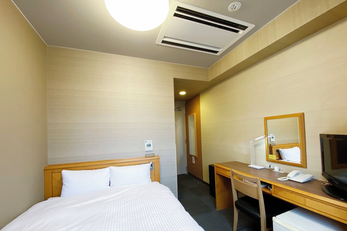 Une chambre d’hôtel équipée d’un lit, d’un bureau, d’une chaise, d’une télévision, d’un miroir et d’un petit réfrigérateur.