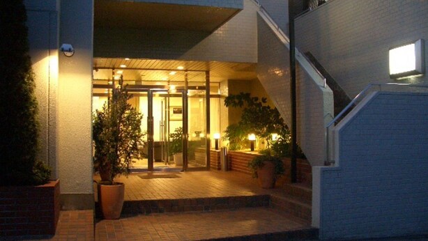 A hotel entrance with a glass door, potted plants, and a staircase leading to the upper floor. - Hotel Route Inn Hitachitaga (Hitachi)