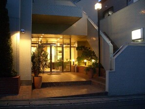 A hotel entrance with a glass door, potted plants, and a staircase leading to the upper floor.