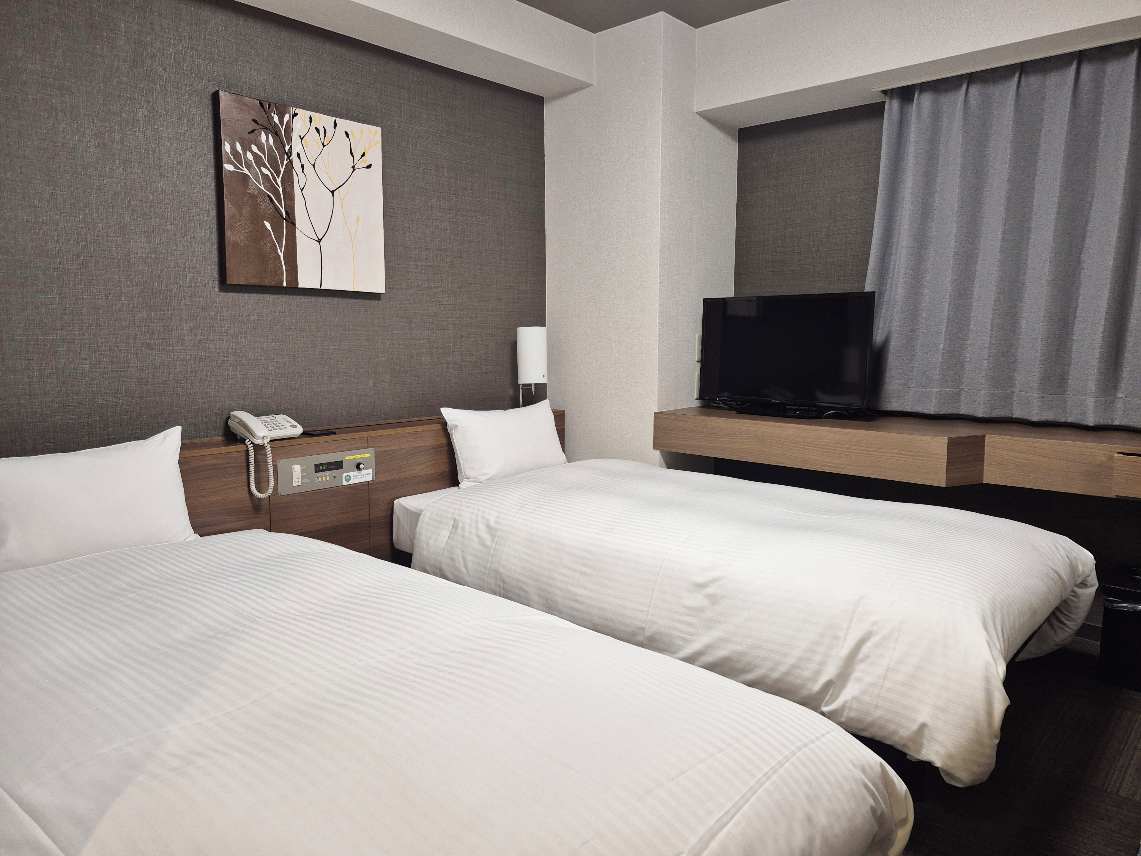 Ein Hotelzimmer mit zwei Betten, einem Nachttischtelefon, einem Flachbildfernseher und einem Bild an der Wand.