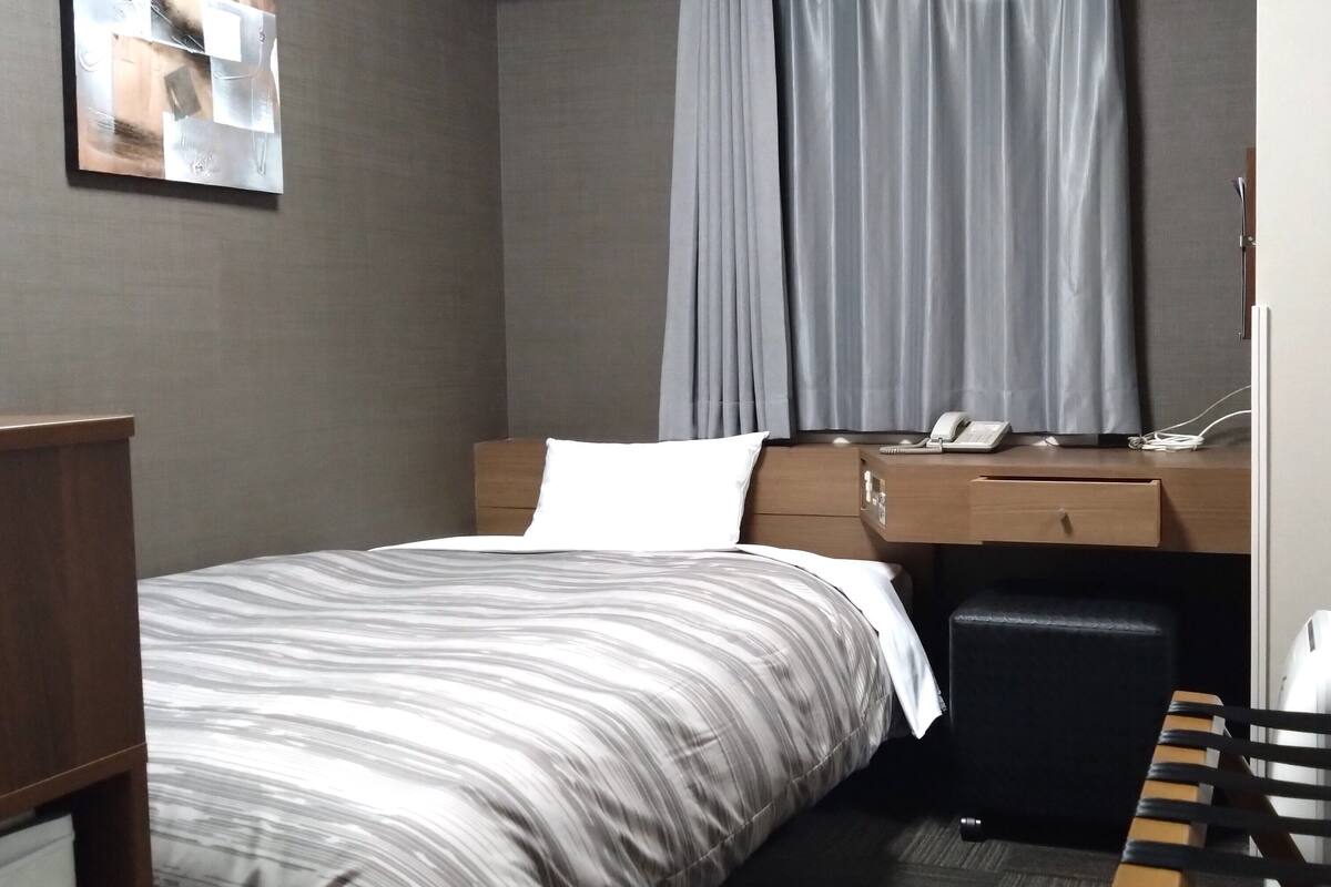 A hotel room with a bed, a desk, a chair, a telephone, and a small table.