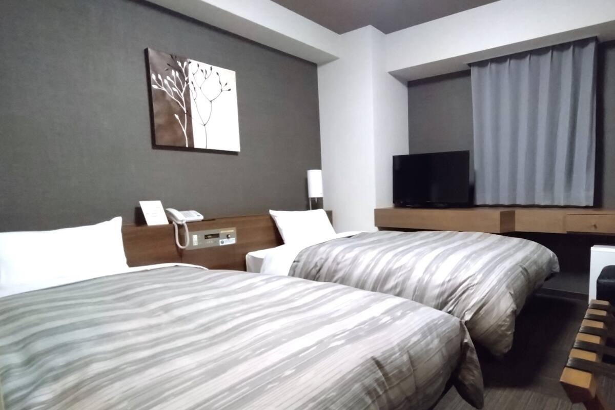 A hotel room with two beds, a flat-screen TV, a bedside table with a phone, and a painting on the wall.