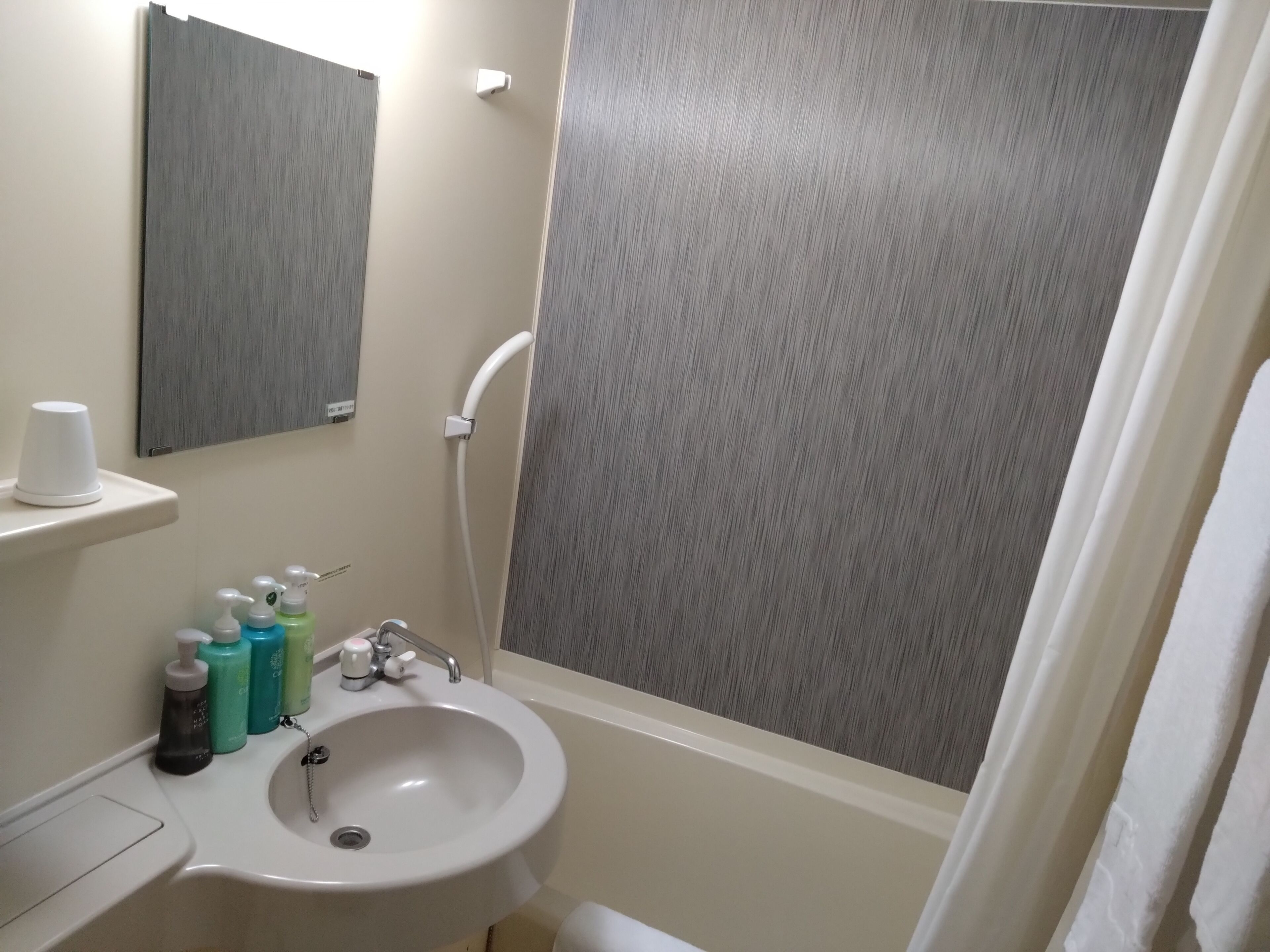 A bathroom with a sink, mirror, shower curtain, and toiletries.