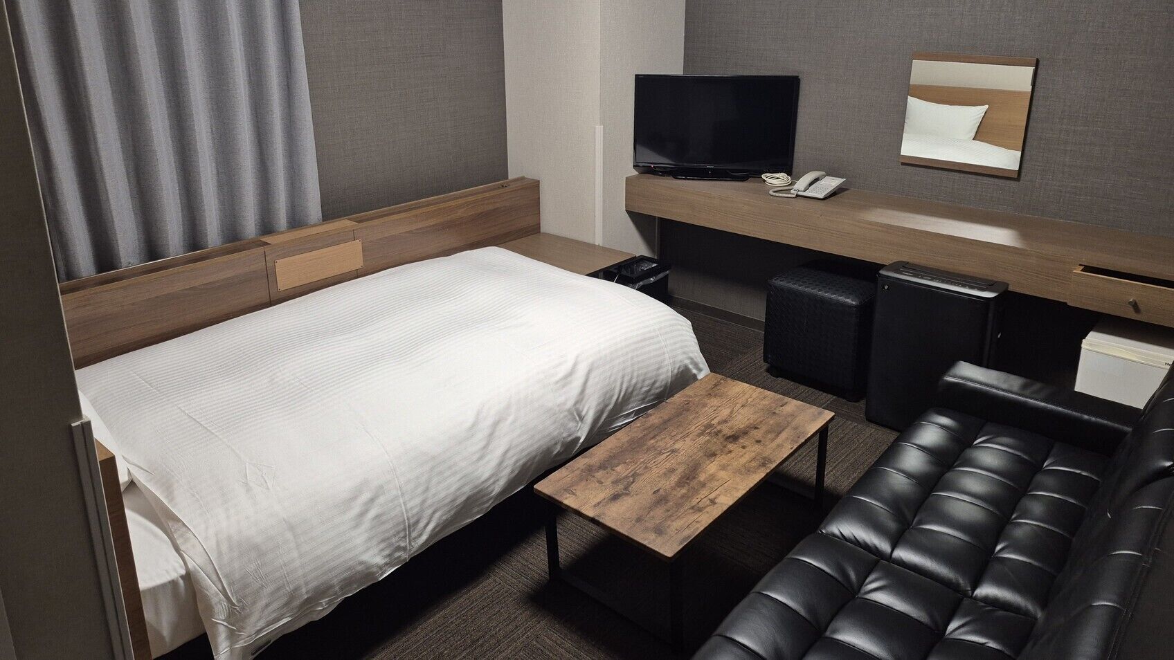 Habitación de hotel con cama, escritorio con televisor, sofá y una mesita.