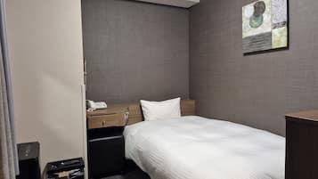 A hotel room with a single bed, a wooden nightstand, a telephone, a black leather chair, a small table, and a wall-mounted artwork.