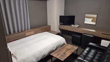 A hotel room with a bed, a desk, a television, a small table, and a leather sofa.