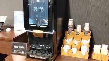 A self-service coffee station with a digital display, coffee pods, and a sign indicating operating hours.