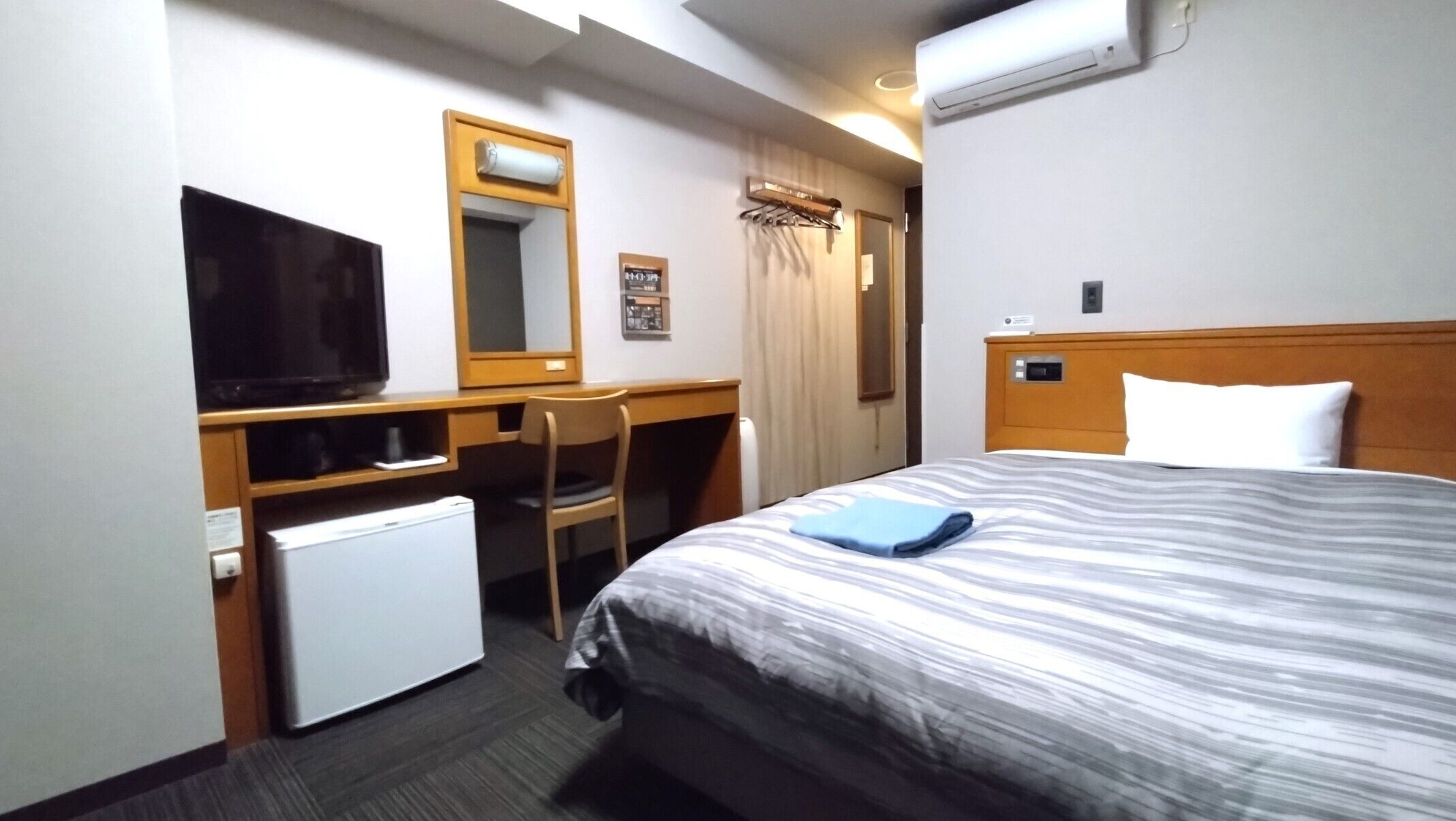 Habitación de hotel con cama, escritorio, silla, televisor y refrigerador pequeño.