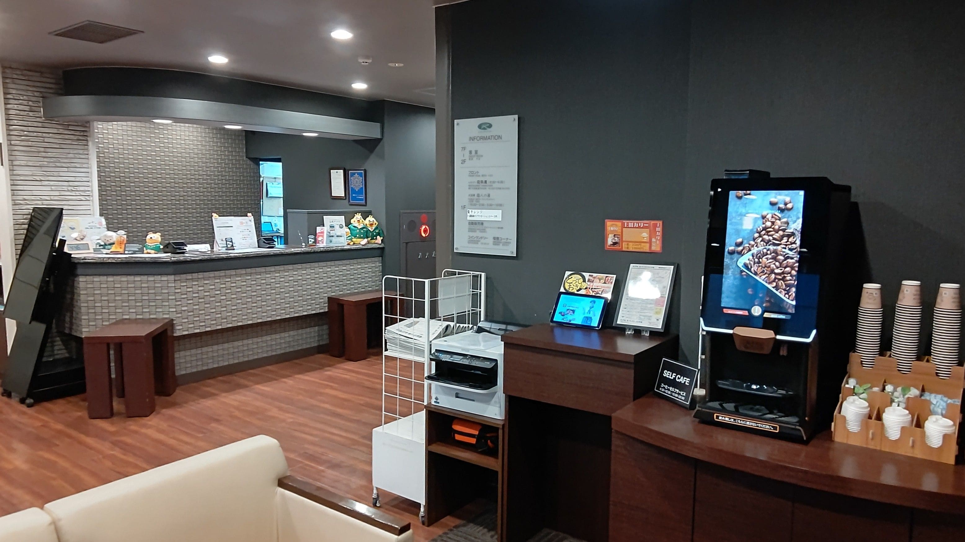 A self-service coffee station with a digital menu display, a coffee machine, and a counter with a menu board.