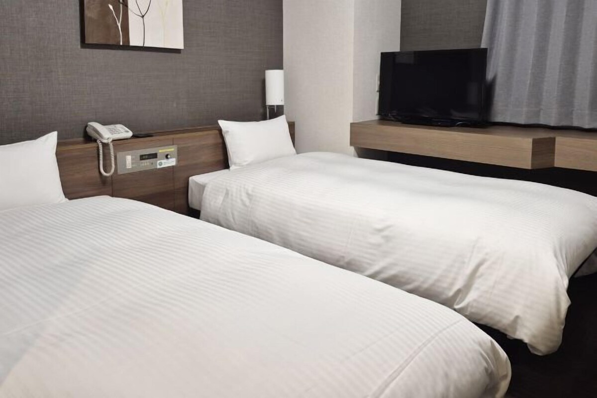 A hotel room with two beds, a TV, a phone, and a lamp.
