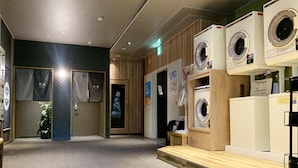 A laundry facility with multiple washing machines, a wooden counter, and a tiled floor. - Hotel Route Inn Hitachitaga (Hitachi)