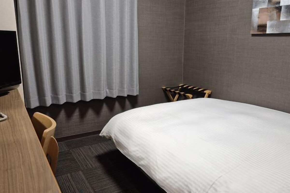 A hotel room with a bed, a desk, a chair, a TV, and a window with curtains.