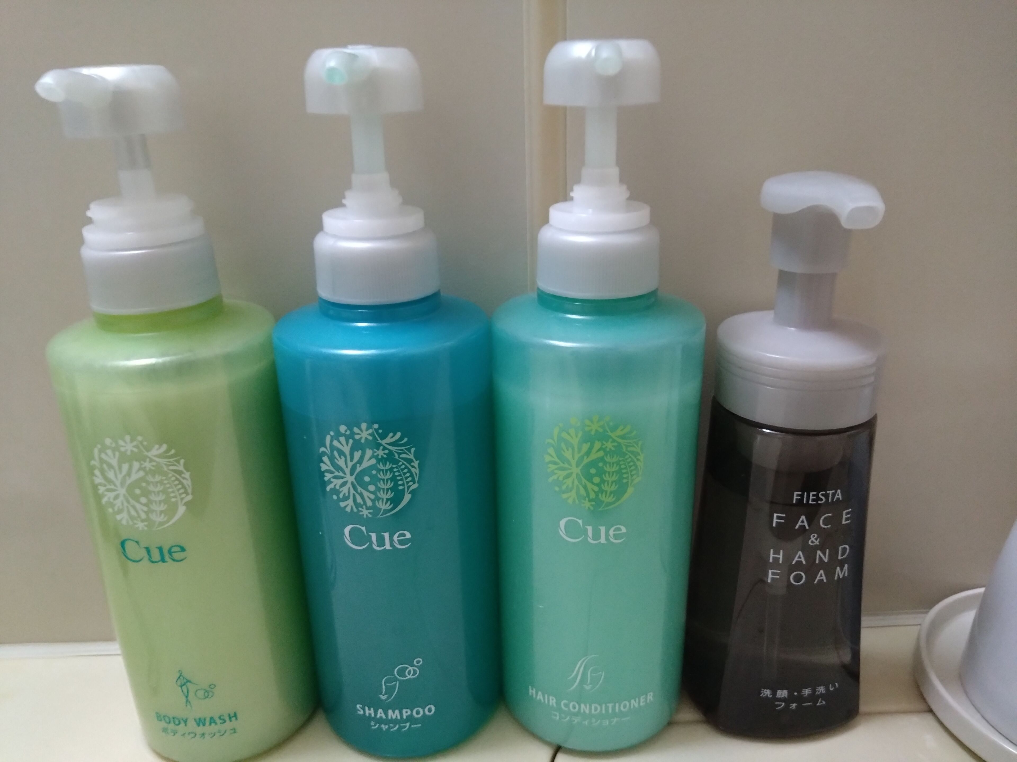 Vier flessen CUE douchegel en haarconditioner op een plank.