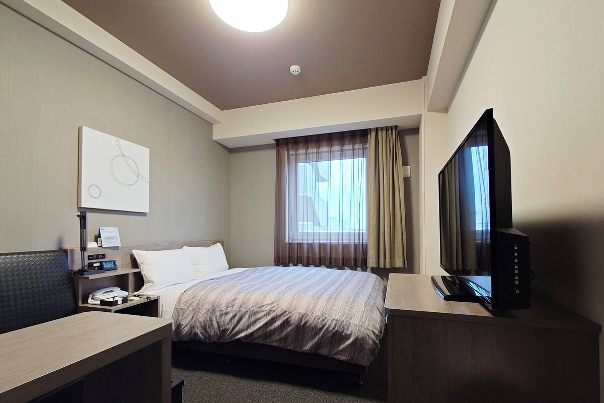 A hotel room with a bed, a desk, a television, and a window with curtains.
